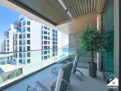 a balcony with two chairs and a potted plant at Seafront Serenity Palm Escape with Pool Access in Dubai