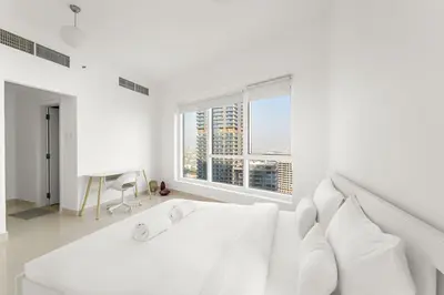 a white bedroom with a large white bed and a window at FIRST CLASS 2BR Cozy City Retreat in Dubai