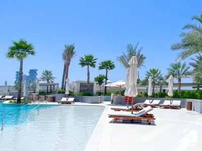 a pool with chairs and umbrellas and palm trees at Luxury Beachfront 1BR on Palm Jumeirah & Balcony in Dubai