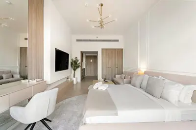 a white bedroom with a large bed and a living room at FIRST CLASS Studio Luxe & Cozy Vibes in Dubai