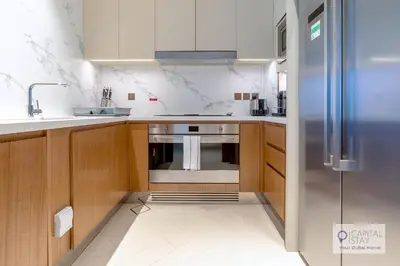 a kitchen with wooden cabinets and a stainless steel refrigerator at Luxury 3BR Apartment with Burj Khalifa Views - Address Opera in Dubai