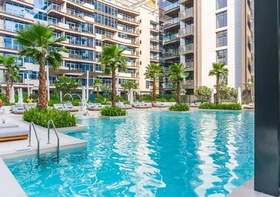 a large swimming pool with palm trees and buildings at Royal Vista - Luxury 1BR Apartments at Kensington Waters in Dubai