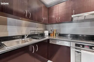 a kitchen with wooden cabinets and stainless steel appliances at bnbme - Luxury Anantara Palm Apt Beachfront Lagoon Pools Balcony & Spa Access in Dubai