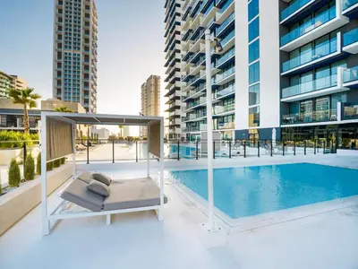 a swimming pool with a bed in front of a building at Vogue JVC Binghatti Corner near Circle Mall, One Bedroom Apartment with Balcony and City View, Access to all Amenities in Dubai