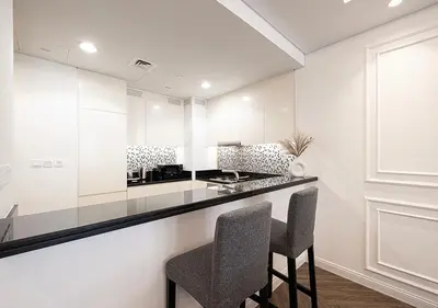 a kitchen with white walls and a counter with two chairs at Paramount Midtown Hotel - Luxury Apartments & Infinity Pool with Burj Khalifa View in Dubai