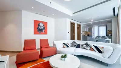 a living room with a white couch and orange chairs at Spacious 2BR, Sobha Waves, Family-Friendly Stay - 3AB11 in Dubai