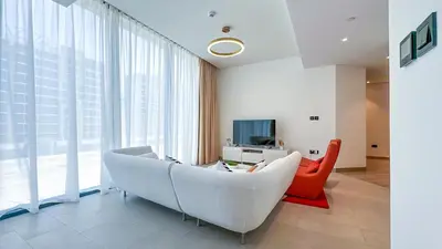 a living room with a white couch and a red chair at Spacious 2BR, Sobha Waves, Family-Friendly Stay - 3AB11 in Dubai