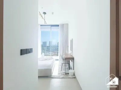 a white room with a desk and a bed and a window at Cozy Luxury l1BR Apartment in Binghatti Amber in Dubai