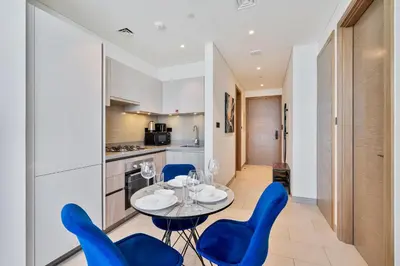 a kitchen and dining room with a table and blue chairs at PVH - Sobha Waves - Serene 1BR minutes to Downtown in Dubai