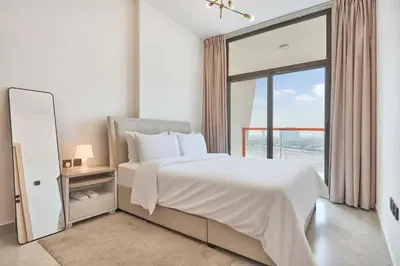 a white bedroom with a large bed and a window at One Bedroom Apartment in Binghatti Avenue by The S Holiday Homes in Dubai