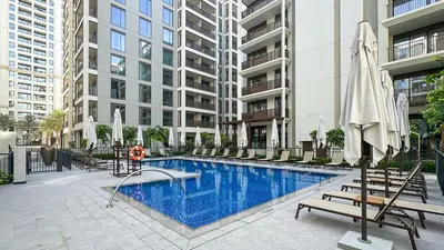 a swimming pool with chairs and umbrellas next to a building at Resort-Style 1BR in Dubai Creek Harbour -1AB01 in Dubai