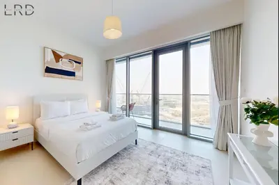 a white bedroom with a bed and large windows at Elegant 2BR with Maids and Stunning Canal Views in Dubai