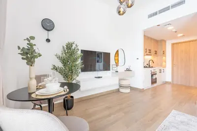 a living room with a table and a kitchen at New Studio Close to Town Square Park, Short Drive to Al Qudra Lake, Liva Apartments by Deluxe Holiday Homes in Dubai