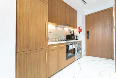 a kitchen with wooden cabinets and a washer and dryer at Pool and Community View Studio, Near Top Landmarks, Azizi Riviera 59, Al Merkadh by Deluxe Holiday Homes in Dubai