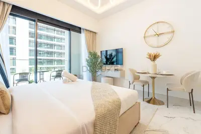 a white bedroom with a large bed and a table at Pool and Community View Studio, Near Top Landmarks, Azizi Riviera 59, Al Merkadh by Deluxe Holiday Homes in Dubai