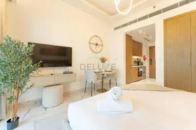 a white living room with a television and a table at Pool and Community View Studio, Near Top Landmarks, Azizi Riviera 59, Al Merkadh by Deluxe Holiday Homes in Dubai