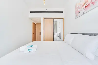 a white bedroom with a bed with a sign on it at FAM Living Minimalist 1BR Gem in Binghatti Amber in Dubai