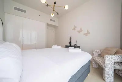 a white bedroom with a large bed and a chair at Zapbed House -Stylish 1 BR Apartment Downtown Views II Tower 2 in Dubai