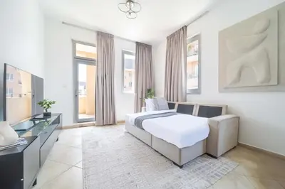 a white bedroom with a bed and a dresser and windows at Cozy 1BR in the Peaceful Community of Motor City in Dubai