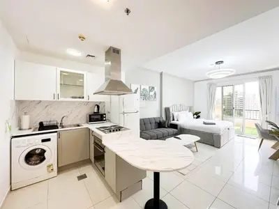a white kitchen with a stove top oven next to a living room at Fully Furnished Studio at Spring Oasis in Dubai Silicon Oasis in Dubai