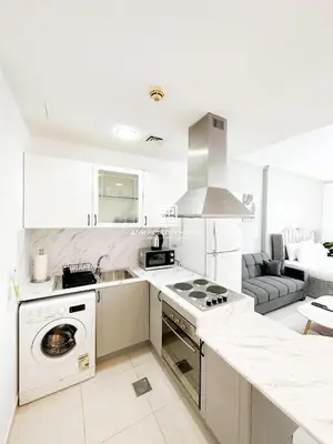 a white kitchen with a stove top oven next to a couch at Fully Furnished Studio at Spring Oasis in Dubai Silicon Oasis in Dubai