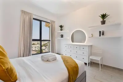 a white bedroom with a bed and a window at Serene 1BR Stay with Pool, Gym, & Kids Playground in Dubai