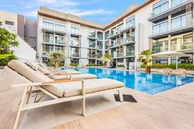 an apartment building with a pool and two lounge chairs at Stylish Studio Near Miracle Garden - Luxury Amenities & Style in Dubai