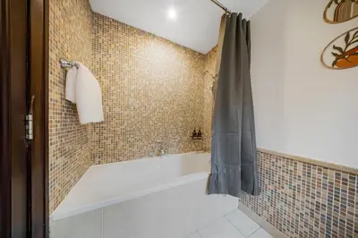 a bathroom with a tub and a tiled wall at Durrani Homes - Zaafaran Luxe Stay Iconic Burj View in Dubai