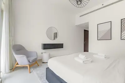 a white bedroom with a bed and a chair at Silkhaus Lavish 2BDR in Bay Square at Prime location in Dubai