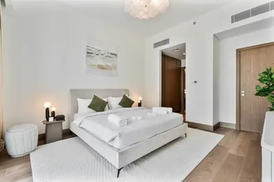 a white bedroom with a large bed and a white rug at Stylish 1 BR in Canal Front with Pool and Gym Access in Dubai