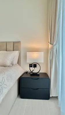 a bedside table with a lamp on it next to a window at Luxury Apartment in Binghatti Amber in Dubai