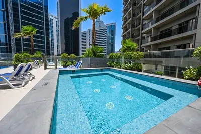 a swimming pool on the roof of a building with chairs and palm trees at Luxury Studio Near Burj Khalifa in Dubai