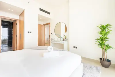 a white bedroom with a large bed and a mirror at High-Floor 1BR with Balcony Overlooking the Lake, Minutes from the Park, Binghatti Onyx, Jumeirah Village Circle by Deluxe Holiday Homes in Dubai