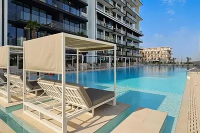 a swimming pool with two lounge chairs and a building at High-Floor 1BR with Balcony Overlooking the Lake, Minutes from the Park, Binghatti Onyx, Jumeirah Village Circle by Deluxe Holiday Homes in Dubai