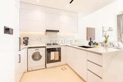 a white kitchen with a washing machine in it at High-Floor 1BR with Balcony Overlooking the Lake, Minutes from the Park, Binghatti Onyx, Jumeirah Village Circle by Deluxe Holiday Homes in Dubai