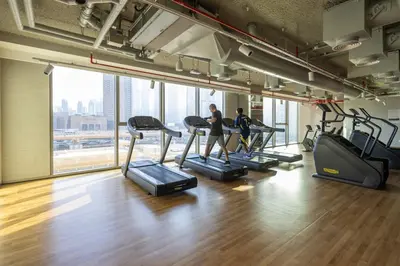 two people running on treadmills in a gym at Maison Privee - Urban & Elegant Stay Just Steps from Burj Khalifa in Dubai