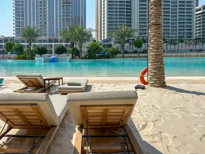 a beach with chairs and a swimming pool with buildings at Elegant at Creek Beach Lotus 1BHK in Dubai