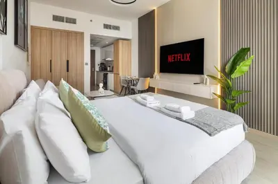 a white bed with pillows and a tv in a room at Luxurious JVC Studio Near Circle Mall & Parks in Dubai
