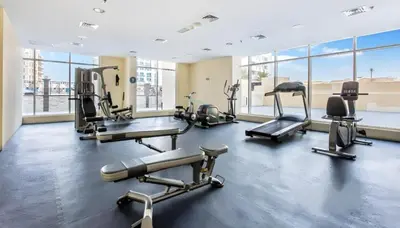 a gym with cardio equipment in a building with windows at Studio with Balcony Facing the Community, Located Near Golf Clubs and Cricket Stadium, Royale Residence 1 , Dubai Sports City by Deluxe Holiday Homes in Dubai