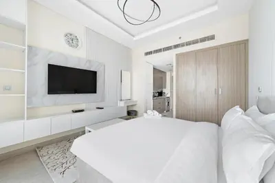 a white bedroom with a large bed and a tv at Farhad Azizi Residence Al Jaddaf in Dubai