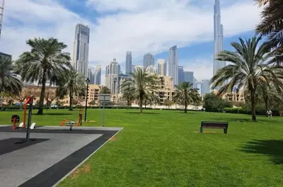 a park with palm trees and a city in the background at Vogue Downtown Bellevue Towers near Burj Khalifa and Dubai Mall, One Bedroom Apartment with City View, Full Access to all Amenities in Dubai
