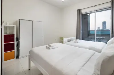 two beds in a white room with a window at Bright 2BR Sports City Near Miracle GardenParks in Dubai