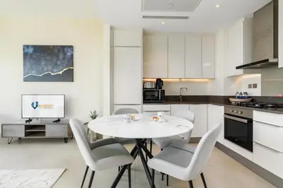 a white kitchen with a white table and chairs at Vacay Lettings - Marina Gate 2 in Sabkhah