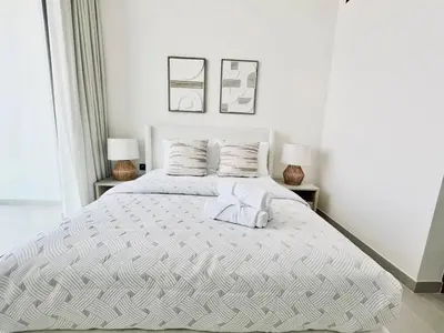 a white bedroom with a large bed with two lamps at Soft Modernity 1br Haven With Parking, Gym & Pool! in Dubai
