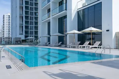 a swimming pool with chairs and umbrellas next to a building at Soft Modernity 1br Haven With Parking, Gym & Pool! in Dubai