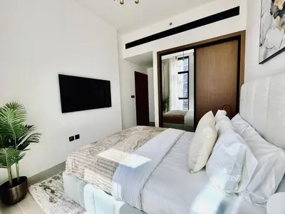 a white bedroom with a large bed and a flat screen tv at Elevated 2br Elegance Dip Pool, Parking And Gym! in Dubai