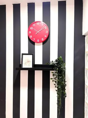 a red clock on a black and white striped wall at Enchanted Stay Partition Room in Barsha Heights in Tecom in Dubai