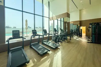 a gym with a row of treadmills and windows at Tranquil 1Bedroom in Binghatti Gardenia in Dubai