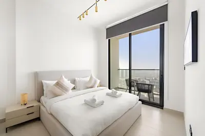 a white bedroom with a large bed and a large window at VayK - Cozy Stylish 1BR in JVC in Dubai