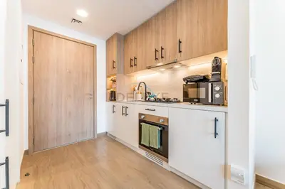 a kitchen with white cabinets and a wooden door at Steps Away from Town Square Park Studio, Minutes Drive to Butterfly Garden, Liva Apartments, Town Square by Deluxe Holiday Homes in Dubai